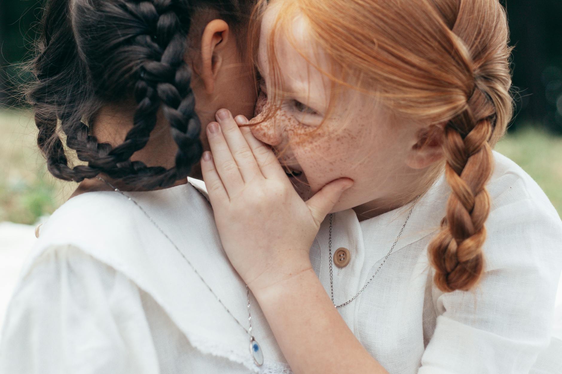 girl whispering to ear of another