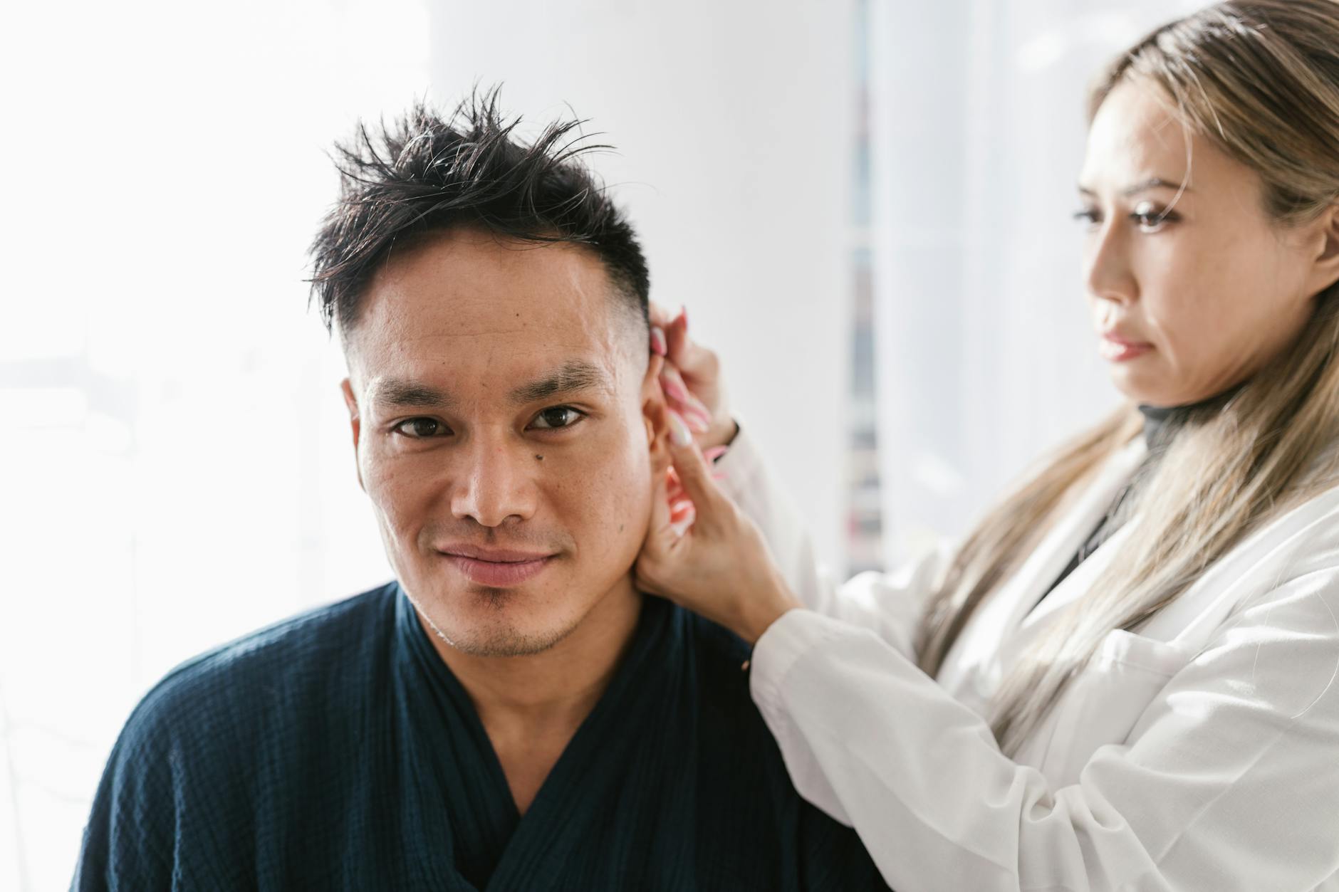 a woman in white laboratory gown looking at a mans ear